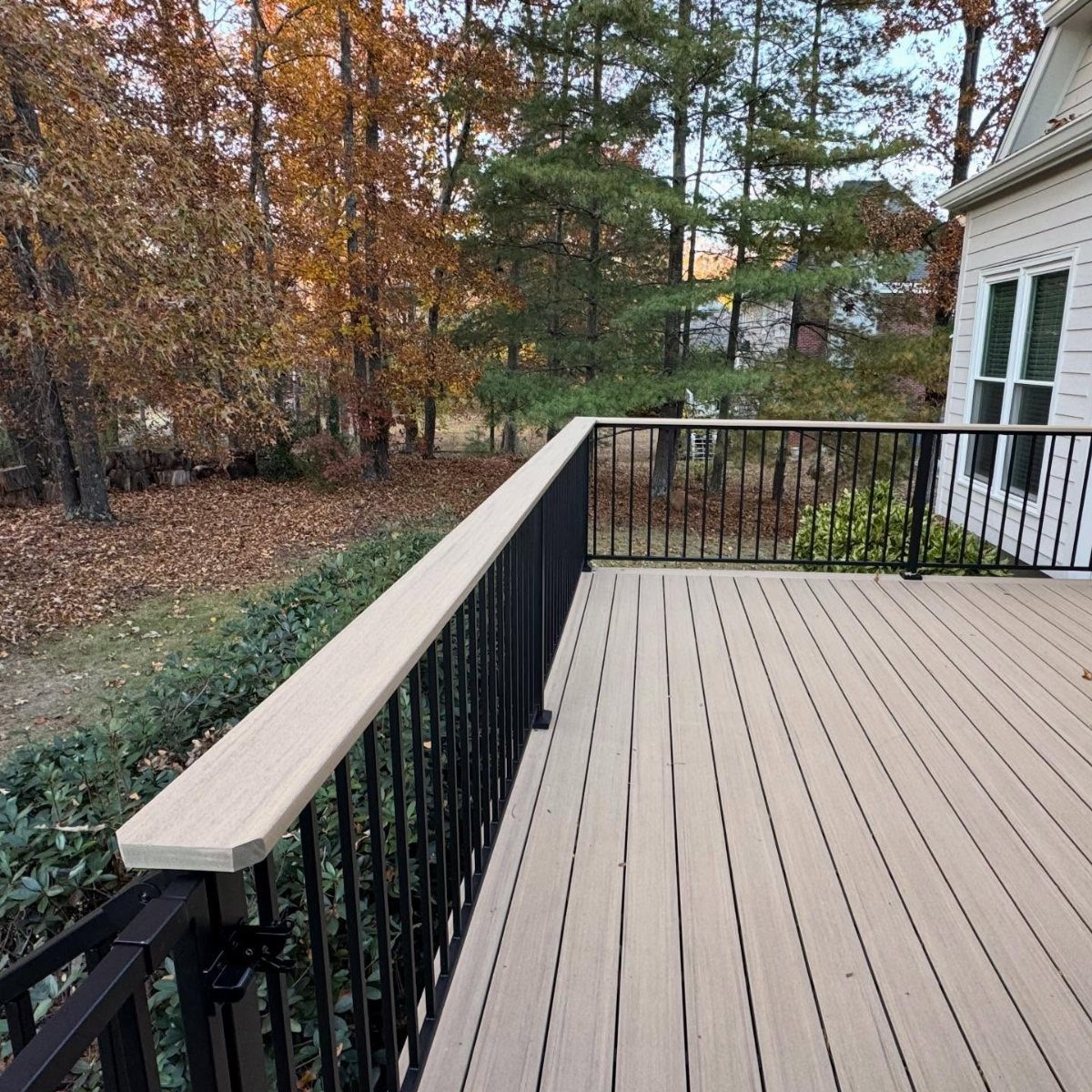 A light tan composite wood deck with black metal railings overlooking autumn trees.