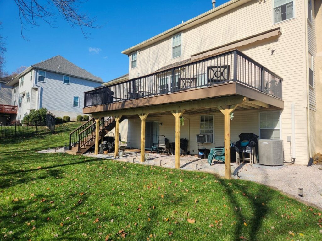 A large wooden second-story deck with black railings attached to a light-colored suburban house.