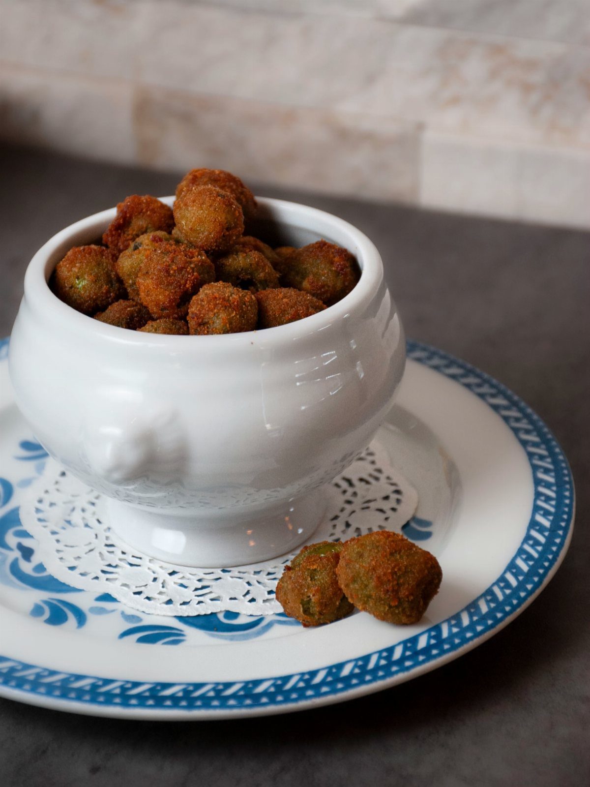 Breaded crispy olives served in a white ceramic bowl on a patterned plate.