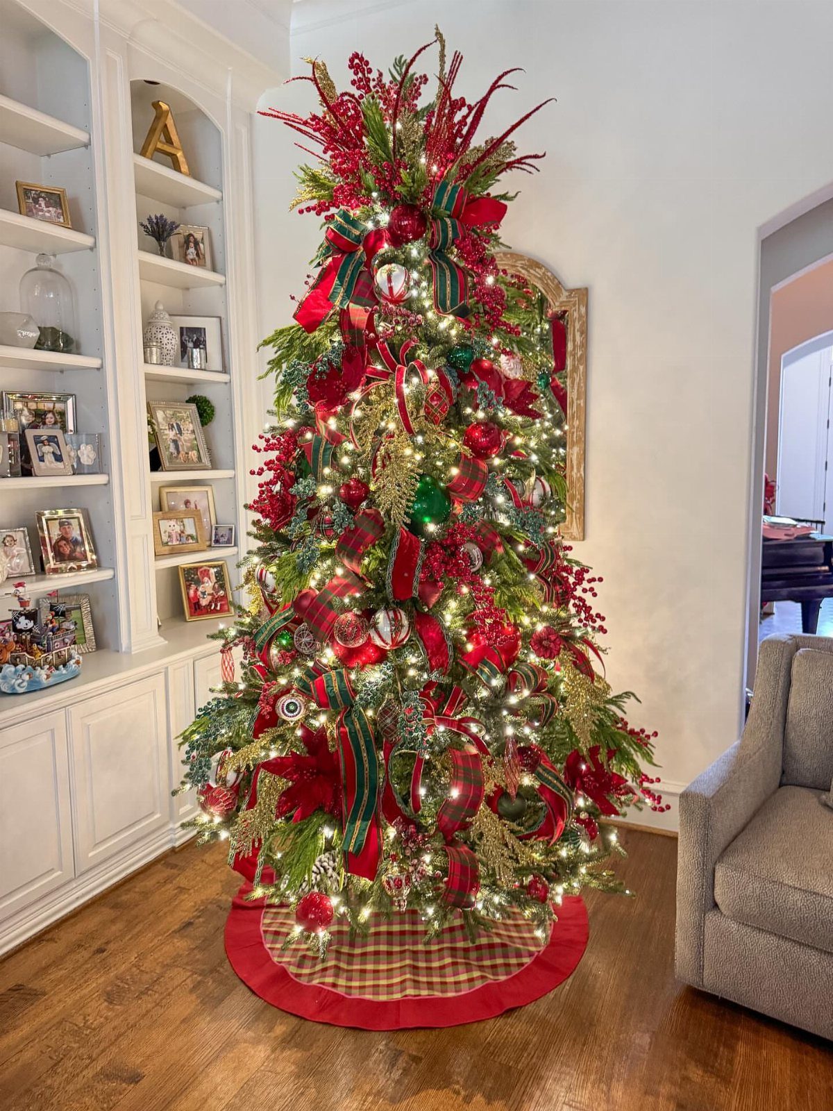 Decorated Christmas tree with red and green ornaments and ribbons standing in a living room.