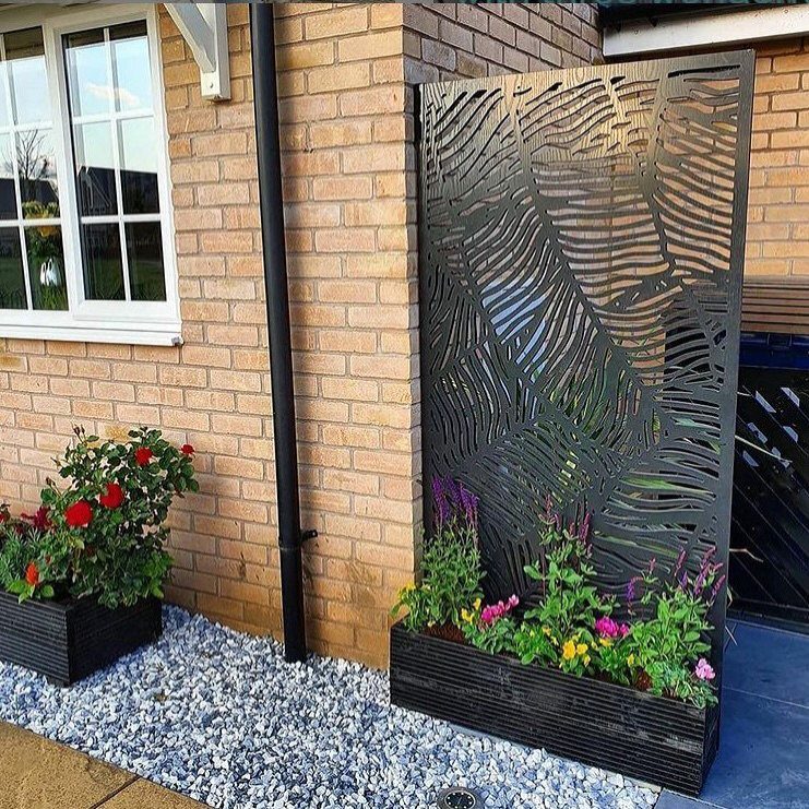 A decorative metal privacy screen with leaf cutouts and a flower planter against a brick wall.
