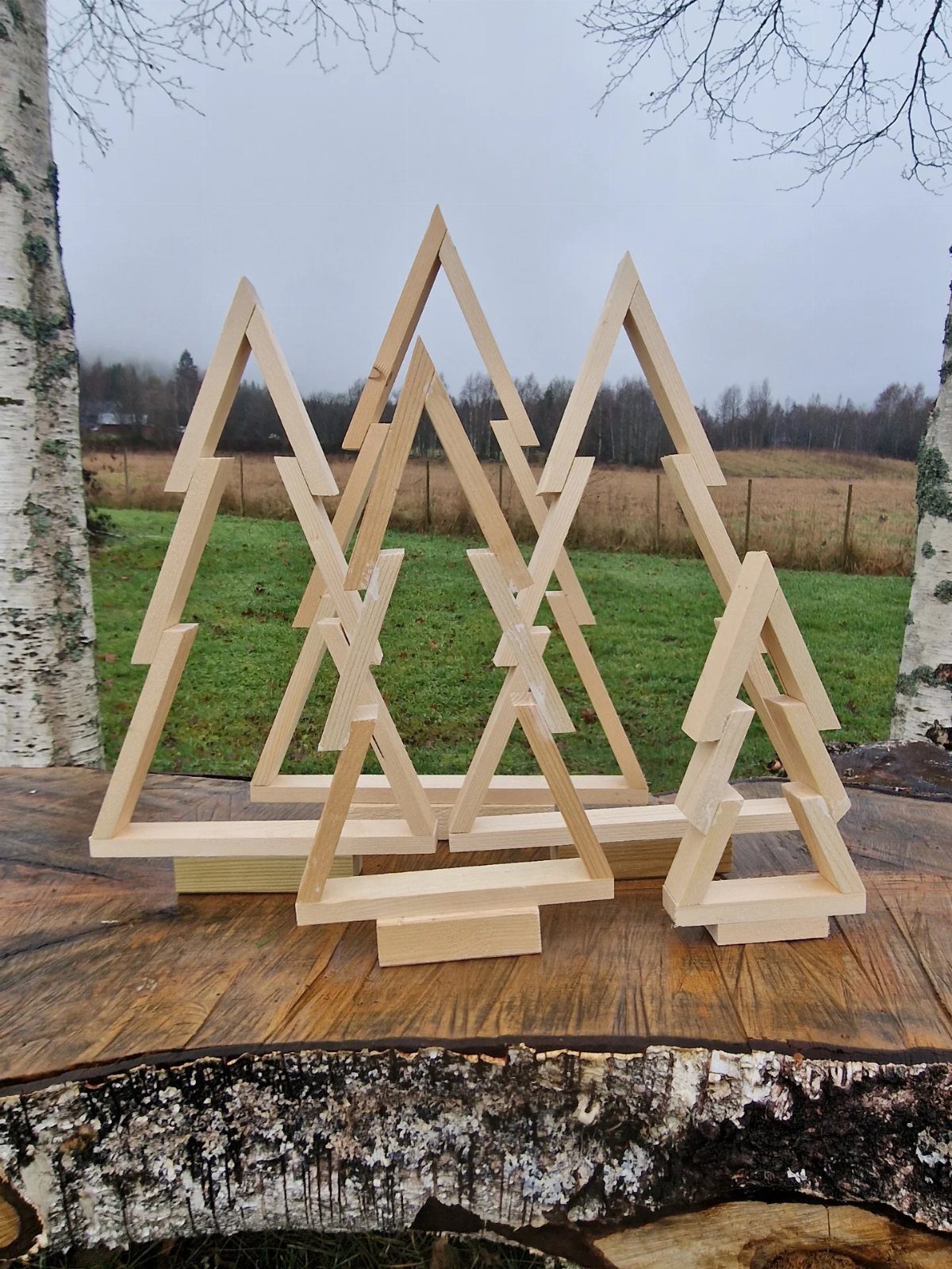 Three minimalist wooden Christmas trees made of light timber slats sitting on a tree stump.